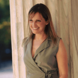 Portrait photo of Sonia Oikonomou standing next to cream colored curtains