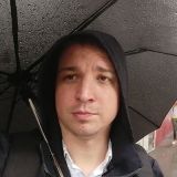 Portrait photo of Dejan Starcevic holding an umbrella in the rain